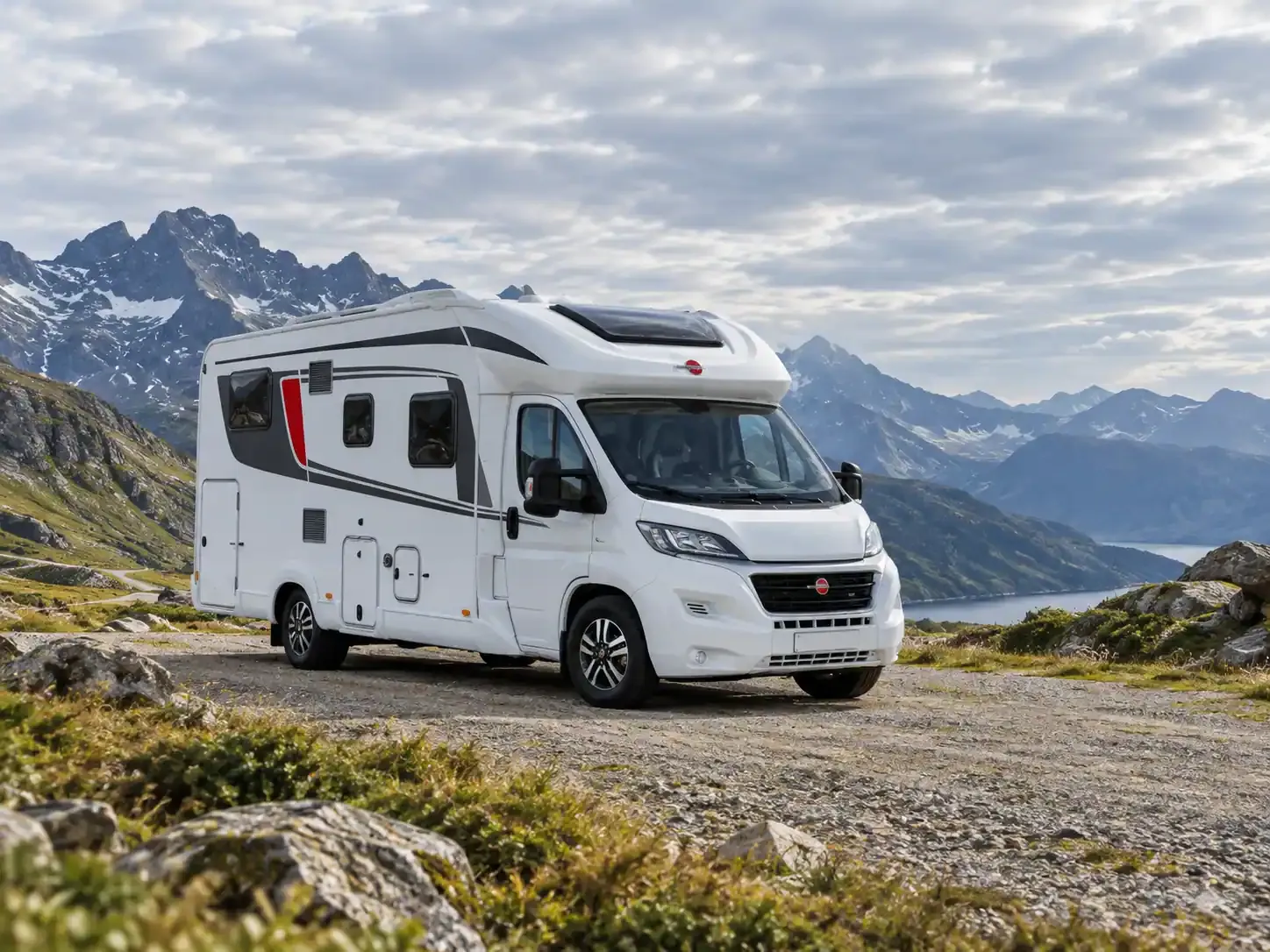 Camping-car sur une aire dégagée, devant des montagnes et un lac