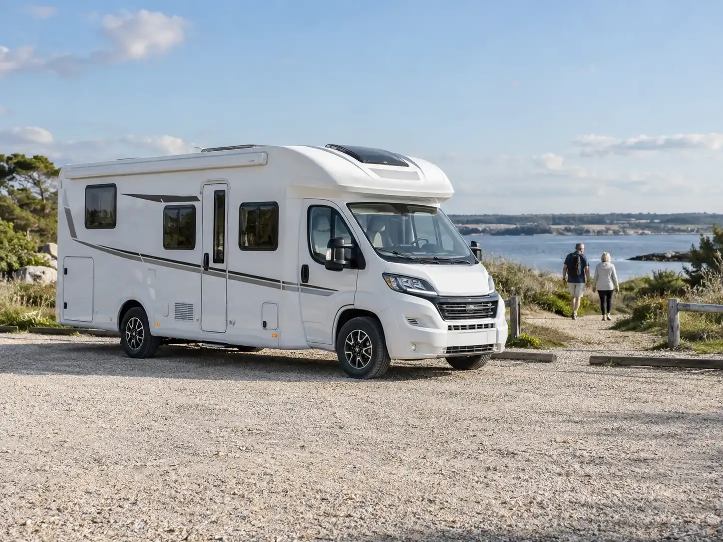 Camping-car au bord de l’eau pendant que deux voyageurs se promènent